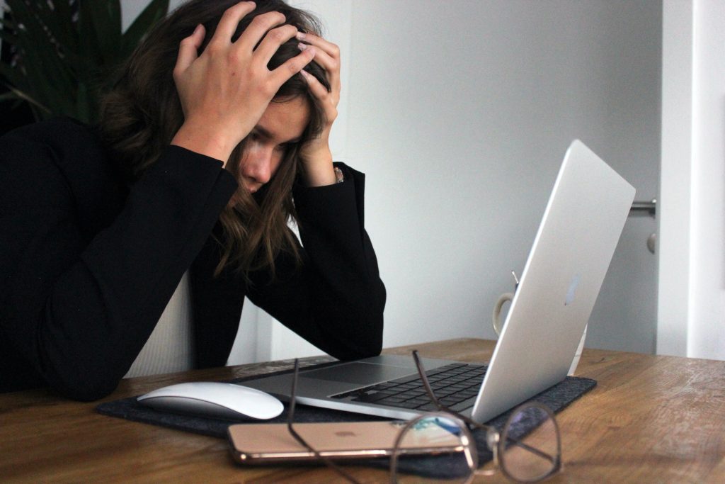 A woman with her head in her hands looking at a laptop. She looks very stressed. 