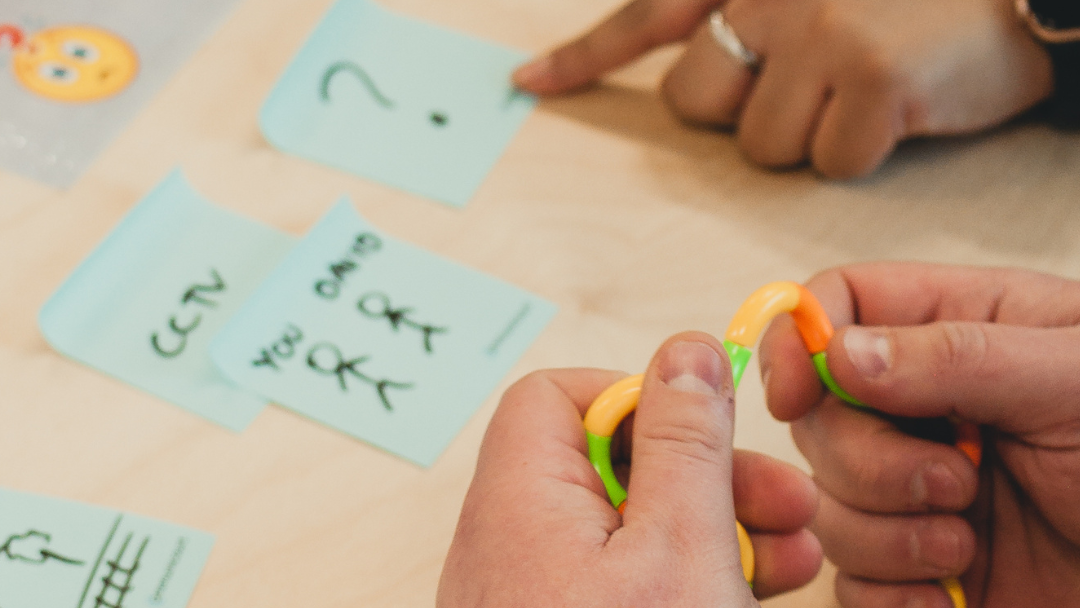 Photo of people hands - an intermediary is helping a court user who is holding a fidget aid while useing a visual timeline and break cards